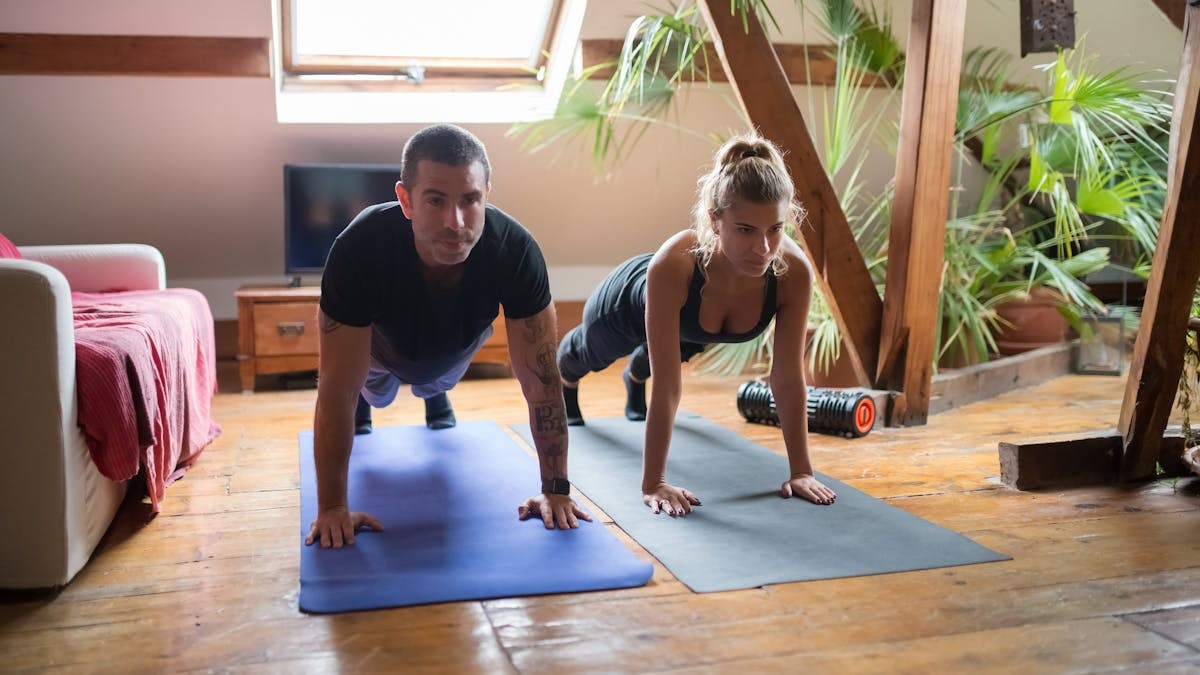 A man and woman doing push-ups together on yoga mats in a cozy home setting.